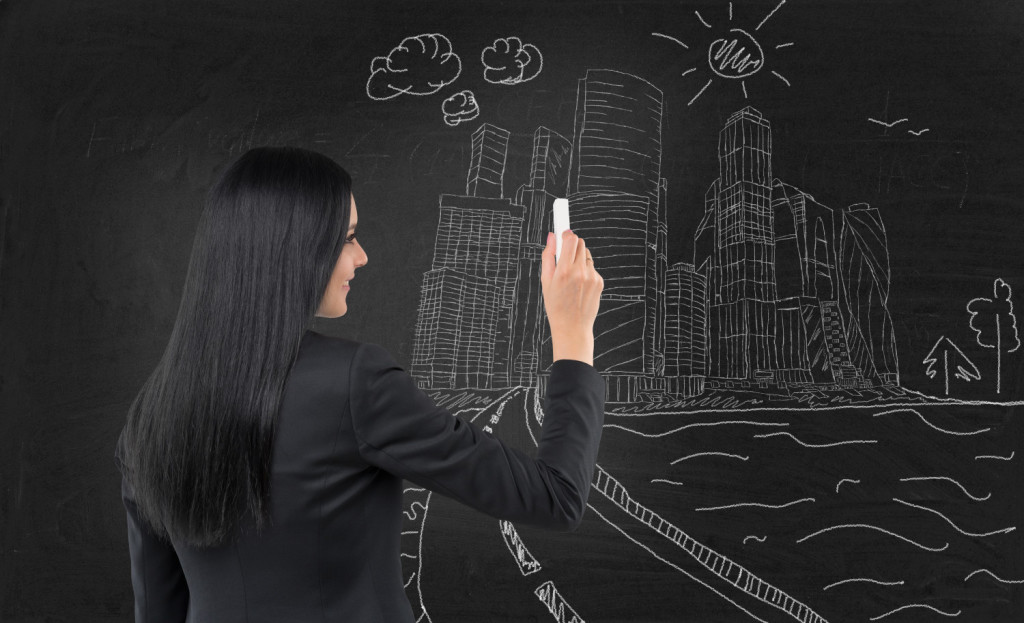 Brunette business lady is drawing a sketch of Moscow International Business Centre, Moscow-city on the black chalkboard.